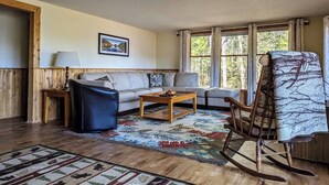 Un salon comprenant un canapé, une table basse, un fauteuil à bascule, un tapis à motifs et un tableau encadré accroché au mur.