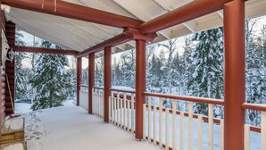 A covered porch with red beams and white railings, leading to a snowy landscape with trees.