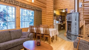 A cozy log cabin interior with a dining area, a fireplace, and a view of snow-covered trees.