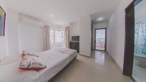 Quarto de hotel com cama, televisão, janela com cortinas e vista para a varanda externa.