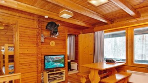 Een houten blokhut van binnen met een houten tafel, een bank en een wandgemonteerde televisie.