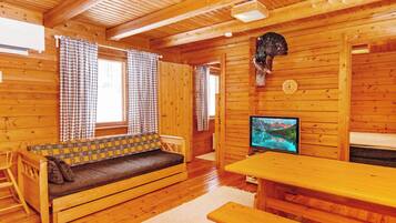 A wooden cabin interior with a sofa, a table, and a television.
