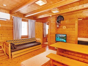 En stuga med träpanel på insidan, inredd med en soffa, ett bord och en tv.