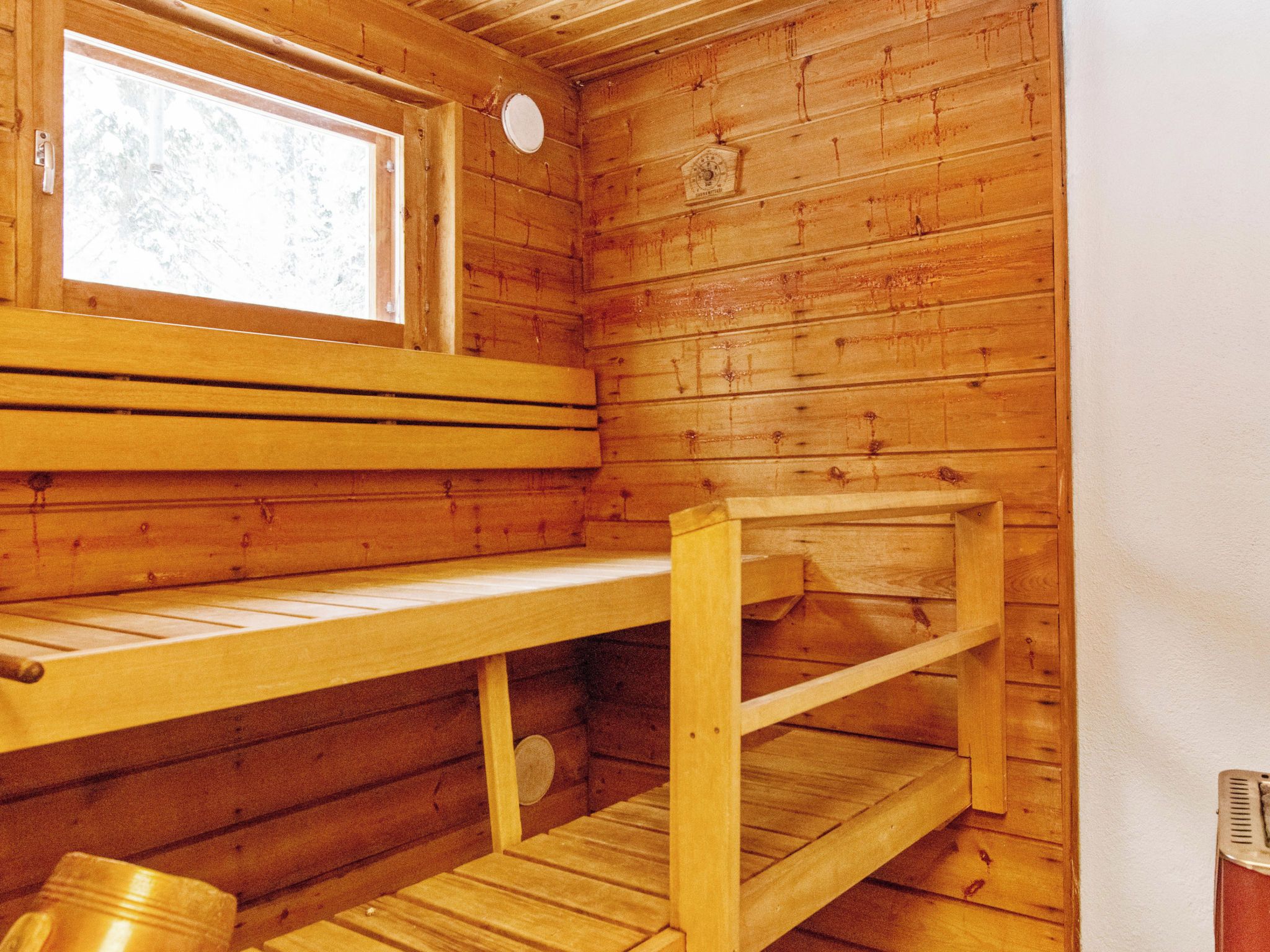A wooden cabin interior with a bench, a shelf, and a window.