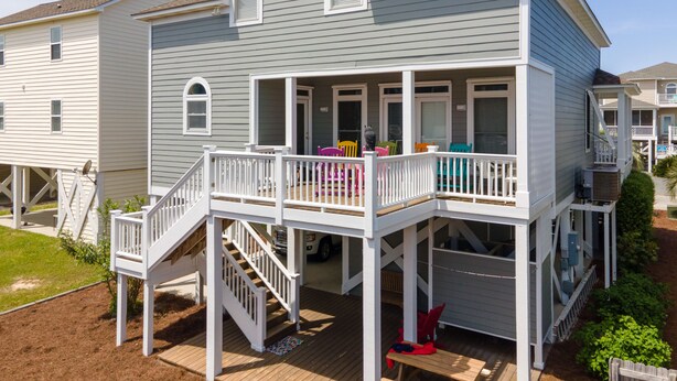 A two-story house with a covered porch, a staircase, and a small deck area. - 4BR beach getaway steps away from the beach with community pool (Ocean Isle Beach)