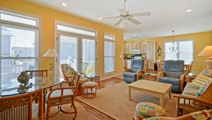 A spacious living room with a glass coffee table, wicker chairs, a blue sofa, and a ceiling fan. - 4BR beach getaway steps away from the beach with community pool (Ocean Isle Beach)