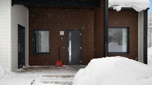 A wooden building with a snow-covered entrance and a red shovel.