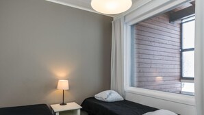 A room with two beds, a nightstand with a lamp, and a window with wooden paneling.