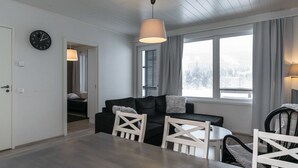 A modern living room with a sofa, chairs, a dining table, and a large window with a view of a snowy landscape.