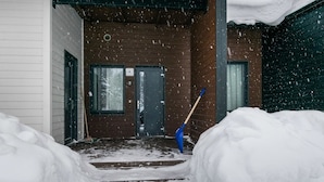 A snowy outdoor area with a wooden door and a blue shovel leaning against it.