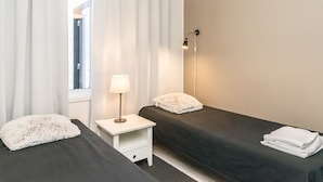A hotel room with two beds, a nightstand, a lamp, and a window with curtains.
