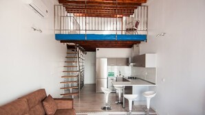 Un apartamento moderno con un dormitorio en entrepiso, una cocina con taburetes de bar y una sala de estar con sofá.