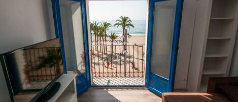 Una habitación con vista a la playa, un televisor sobre un soporte y una cama.