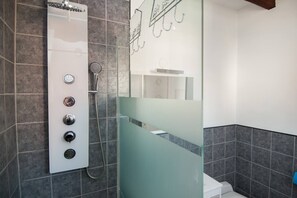 Een moderne badkamer met een douchecabine van glas, een bedieningspaneel aan de muur en een klein spiegelbeeld.