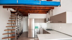 Una cocina moderna con refrigerador de acero inoxidable, gabinetes blancos y una escalera de madera.