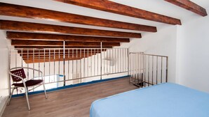 Una habitación con techo inclinado, vigas de madera, barandilla de metal, una cama y una silla.