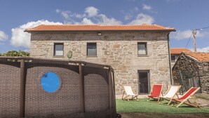 A stone building with a tiled roof, a door, and a small balcony. There are three wooden chairs with cushions on a green lawn in front. - Casa d’El Rey, Serra da Freita/Passadiços do Paiva (Mizarela)