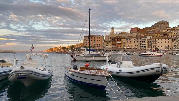 Un port de plaisance avec plusieurs bateaux amarrés, un grand bâtiment avec une tour en arrière-plan et un ciel dégagé.