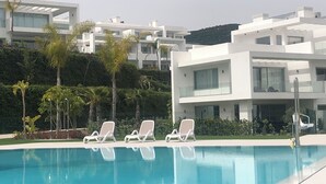 Un espace piscine moderne avec des chaises longues blanches, une piscine à l’eau d’un bleu limpide et des bâtiments contemporains en arrière-plan.