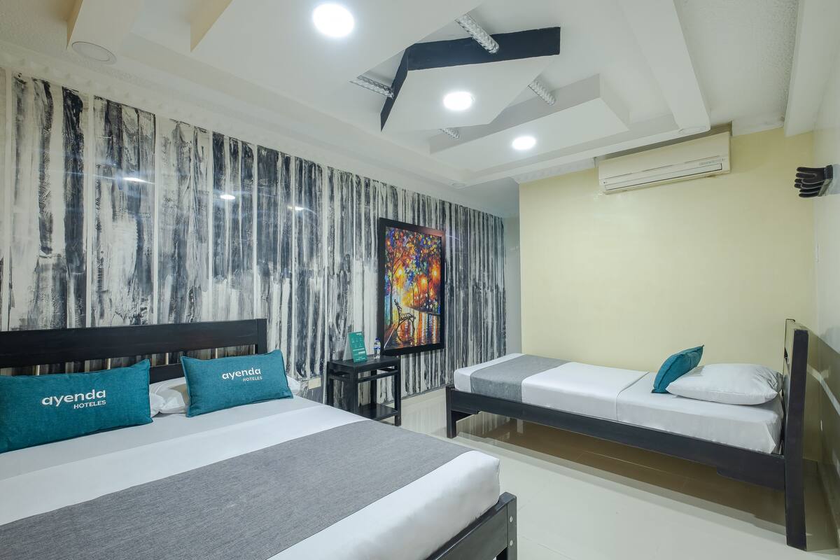 A hotel room with a large bed, a smaller bed, a desk with a chair, and a colorful painting on the wall.