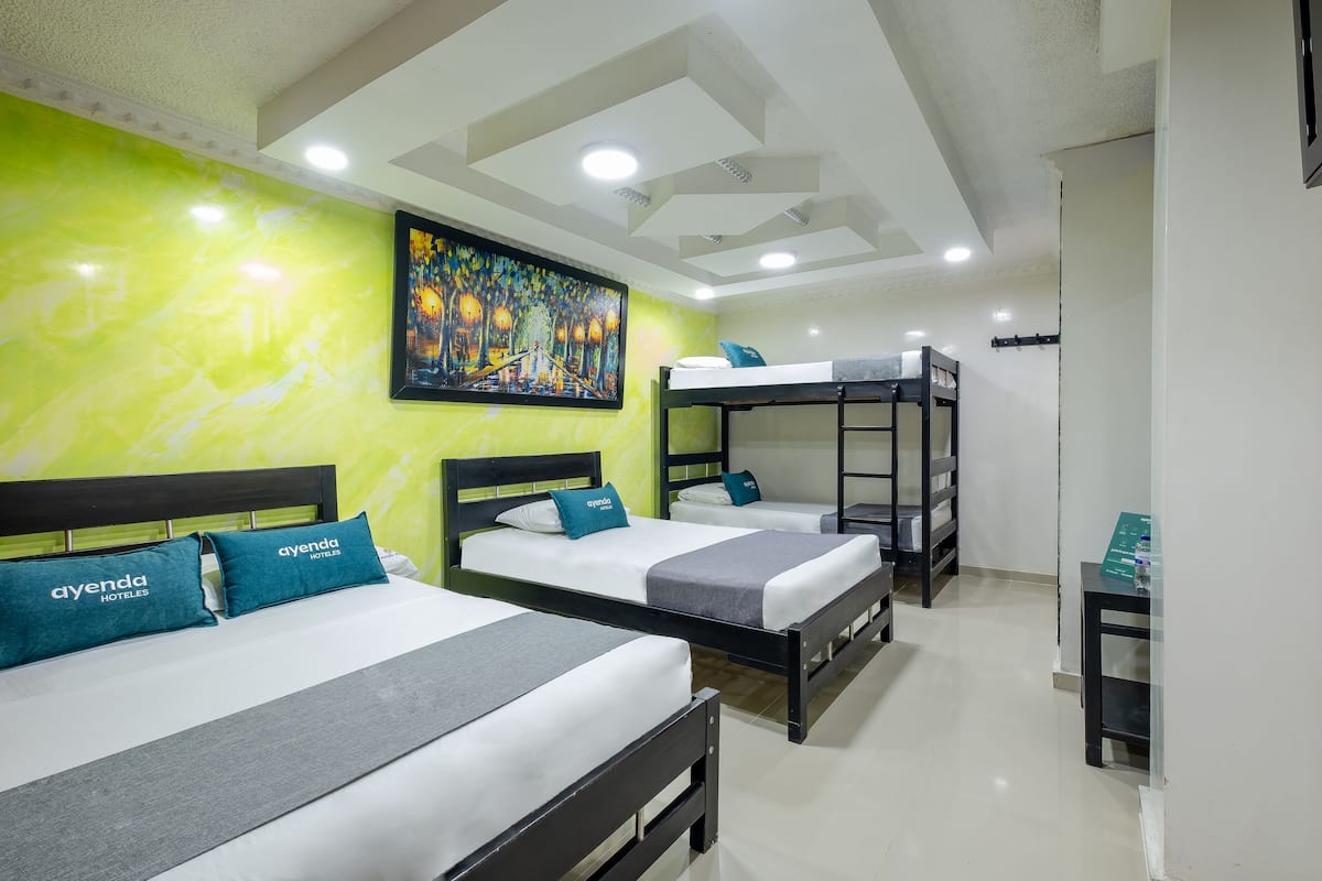 A hotel room with three beds, each with matching pillows, a bunk bed, and a painting on the wall.