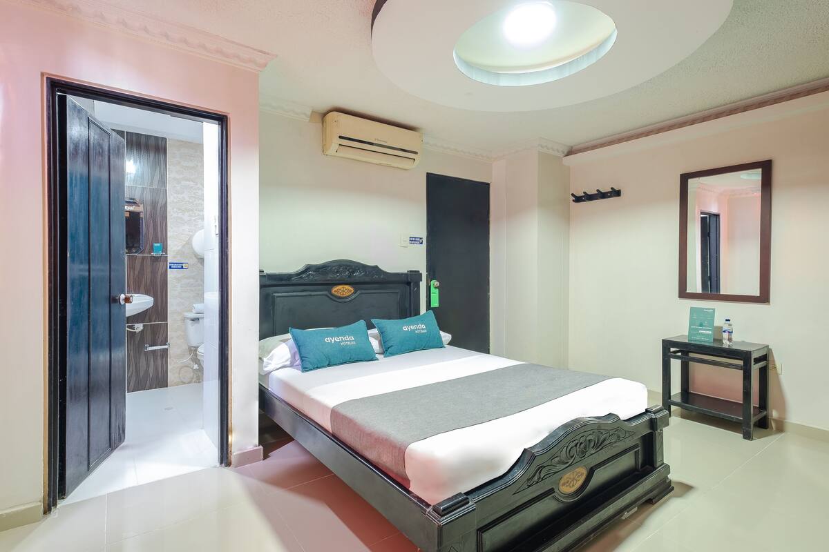 A bedroom with a bed, a bedside table, a mirror, and an air conditioning unit.