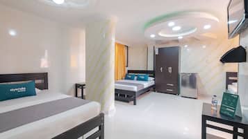 A hotel room with a bed, a desk, a refrigerator, and a TV.