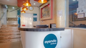 Een receptiegebied van een hotel met een modern design, inclusief een receptiebalie, een klok en een trap naar andere verdiepingen.