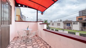 Een balkon met een rode luifel, een kleine tafel met stoelen en vloertegels met een patroon.