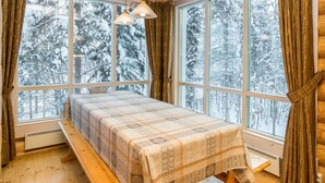 A cozy cabin room with a bed, wooden walls, large windows, and a view of snowy trees. - Hallantähti mökki by Interhome (Hyrynsalmi)