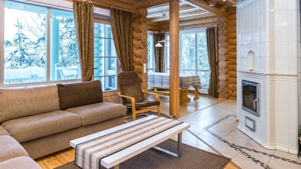 A log cabin interior with a fireplace, wooden beams, a sofa, a dining table, and large windows. - Hallantähti mökki by Interhome (Hyrynsalmi)