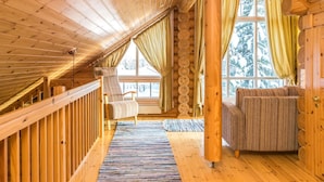 A wooden interior with a sloped ceiling, a sofa, a chair, and a window with curtains. - Hallantähti mökki by Interhome (Hyrynsalmi)