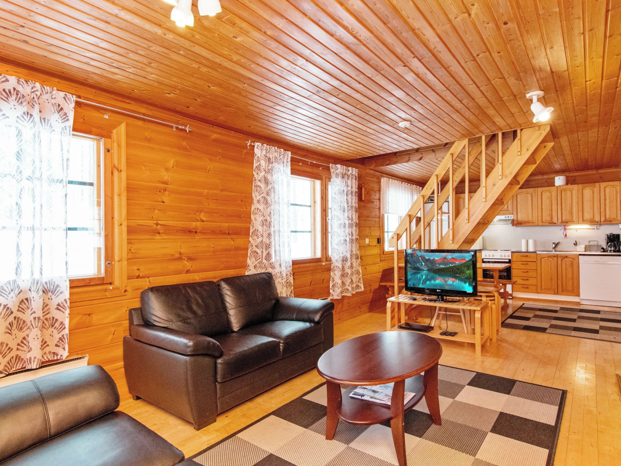 A wooden interior with a sofa, a coffee table, a TV, and a kitchen area.