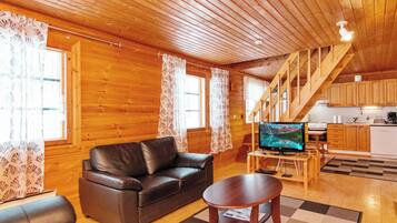 A wooden interior with a sofa, a coffee table, a TV, and a kitchen area.