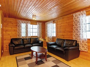 L’intérieur d’un chalet en bois, avec deux canapés en cuir, une petite table et des rideaux à motifs.