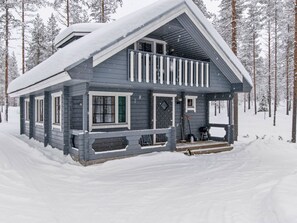 Una cabaña de dos pisos con balcón, rodeada por un bosque nevado.