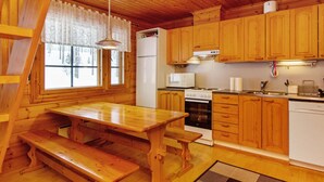A wooden cabin interior with a kitchen area, including wooden cabinets, a refrigerator, a microwave, a stove, and a dining table with benches.