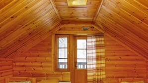 A cozy attic bedroom with wooden walls, a small window, and two beds.