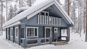 A two-story cabin with a balcony, surrounded by a snowy forest.