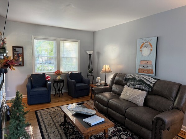 A living room with a brown leather sofa, two armchairs, a coffee table, a lamp, and a painting.