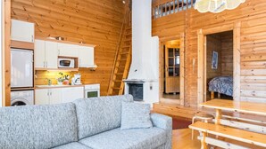 Ein gemütliches Blockhaus-Interieur mit einer Couch, einem Holzespeisesaal, einer Küchenzeile und einem Schlafzimmer auf dem Dachboden.