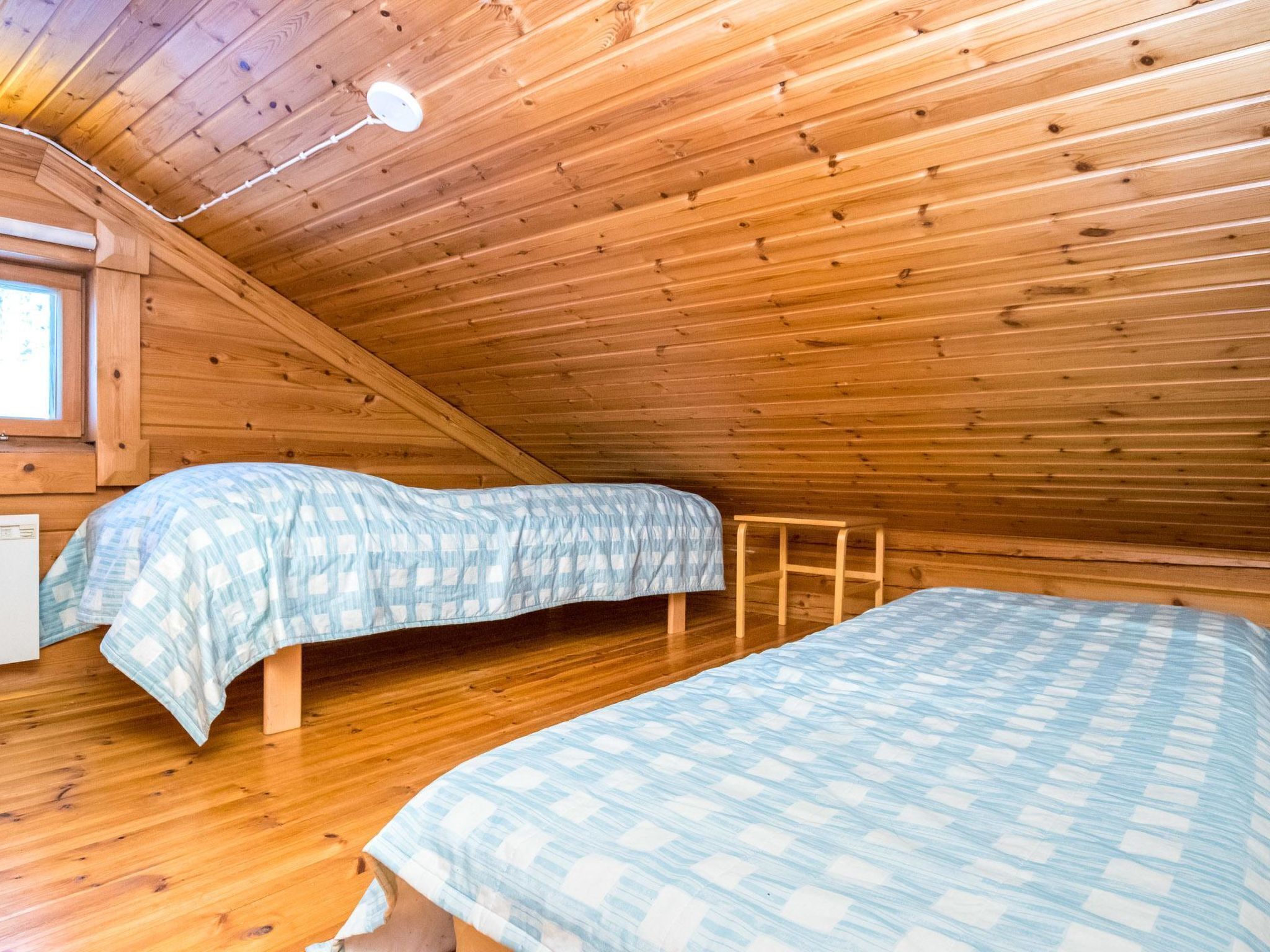 Eine kleine, hölzerne Hütte mit zwei Betten, einem Fenster und einer Deckenleuchte.