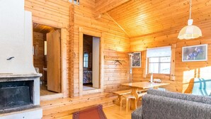 Ein gemütliches Blockhaus-Interieur mit Kamin, Holzwänden, einer Essecke und einer Couch.