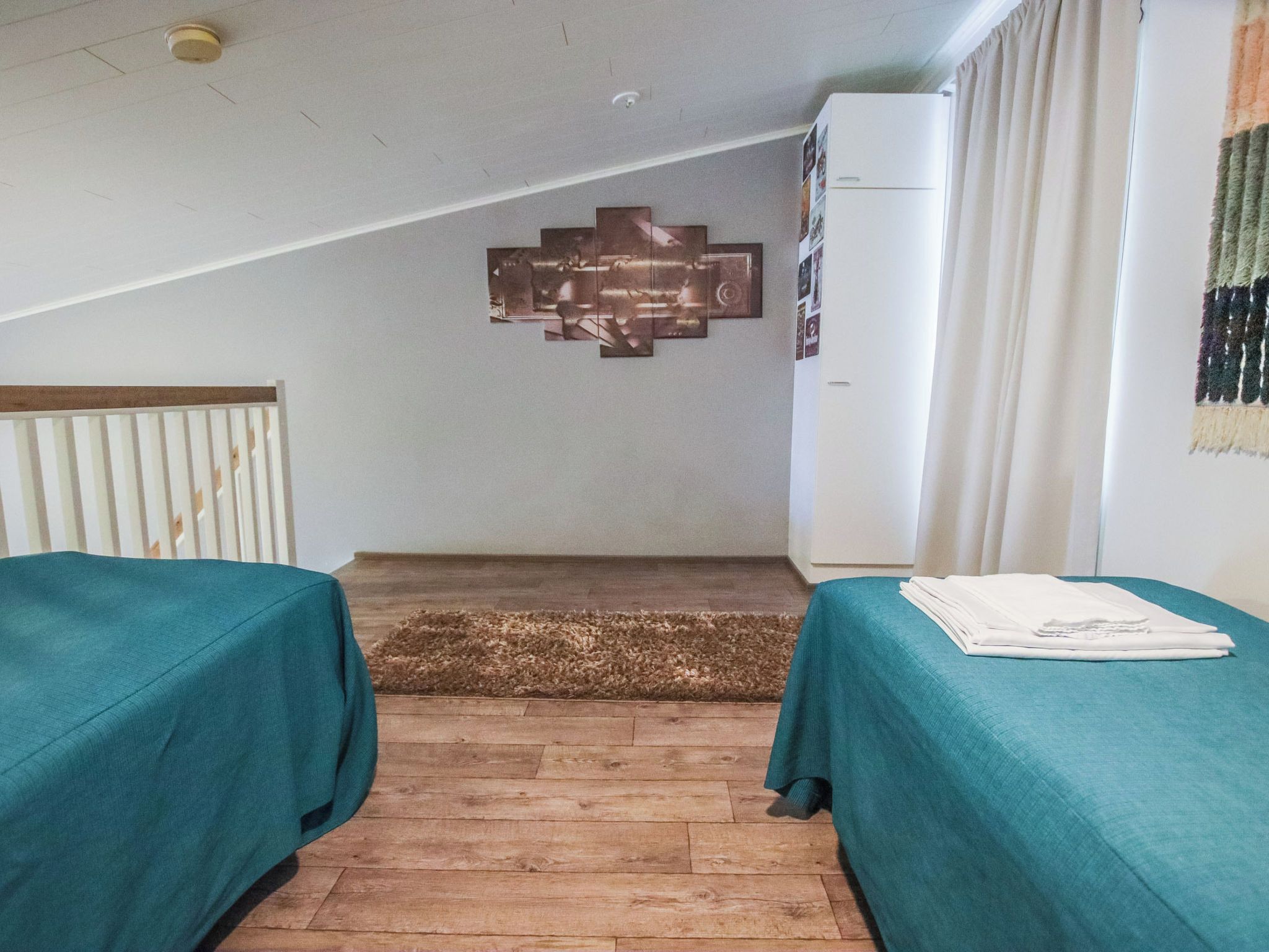 A hotel room with two beds, a wooden floor, a ceiling light, and a wall-mounted decoration.