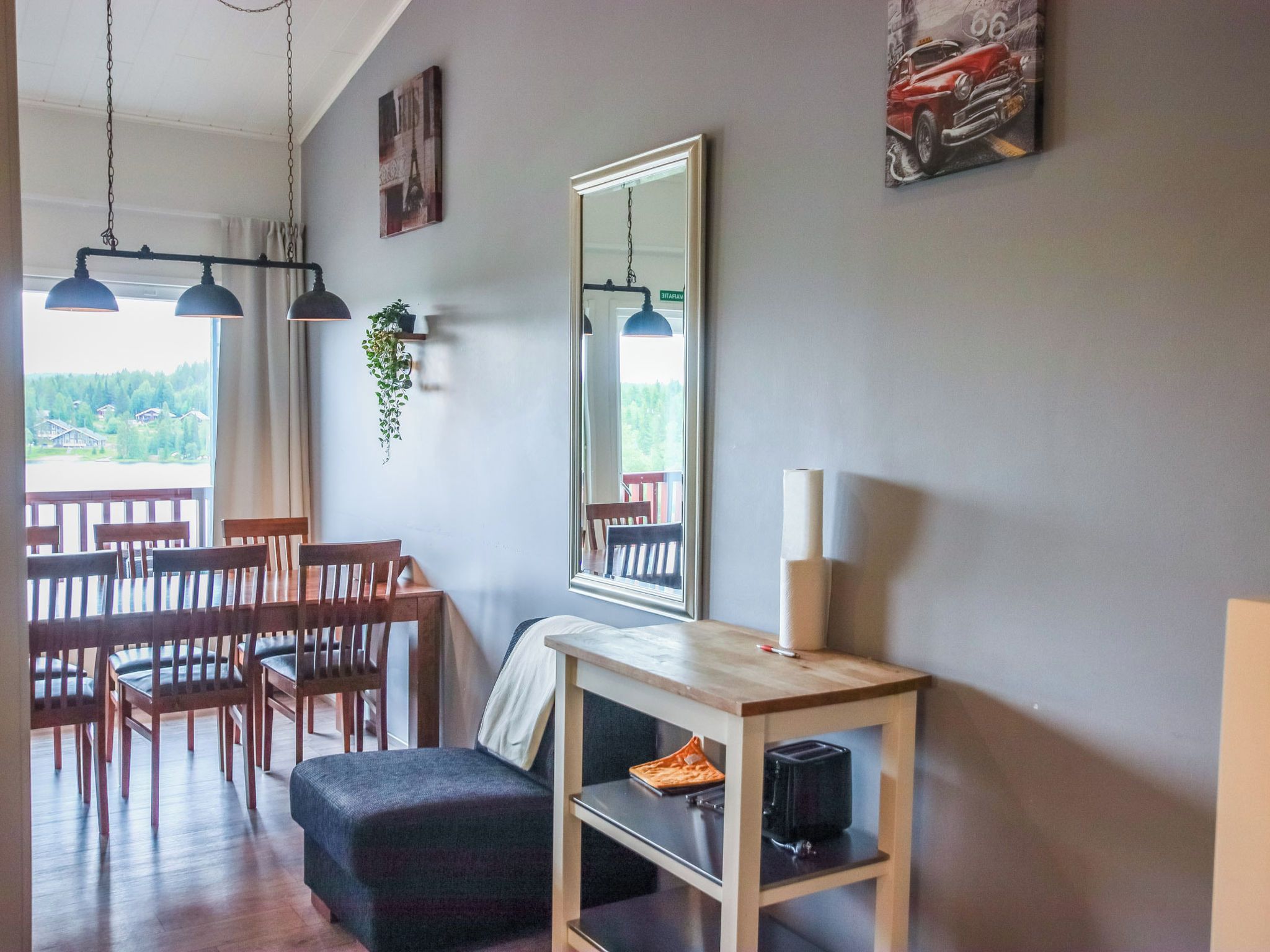 A dining area with wooden chairs and a table, a hanging plant, a mirror, and a painting on the wall.
