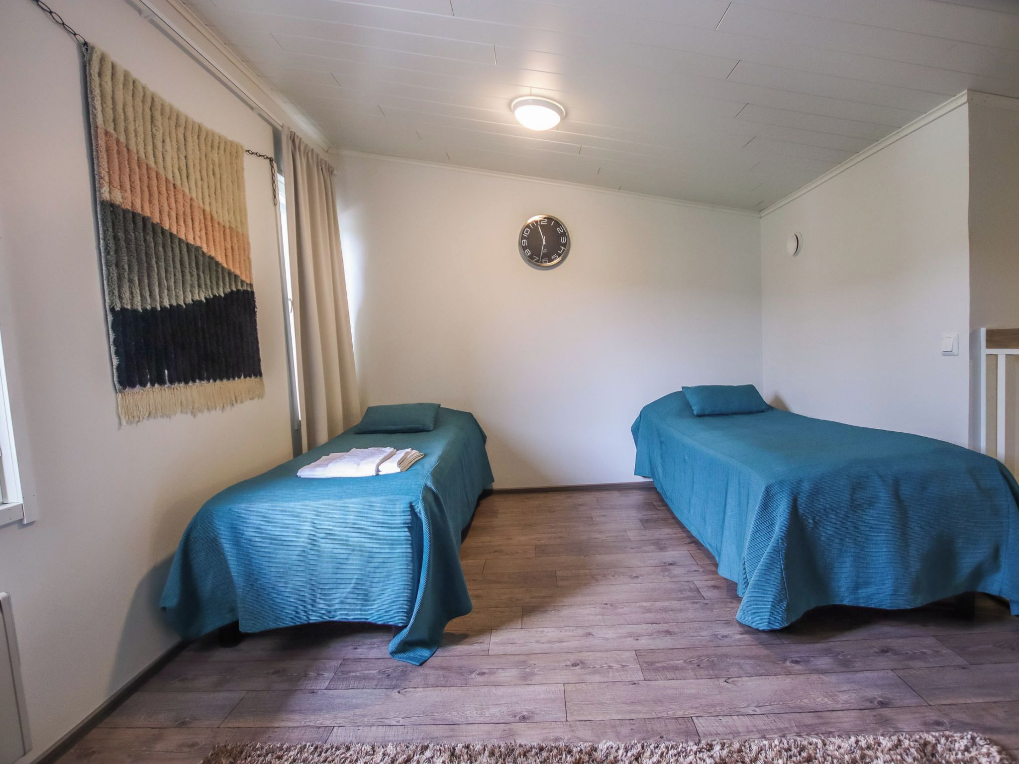 Quarto com duas camas, um relógio na parede e um tapete no chão.