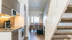 A modern kitchen with built-in appliances, a dining area with a table and chairs, and a wooden staircase. - Skivillas 61 ukkohalla (b3) by Interhome (Hyrynsalmi)
