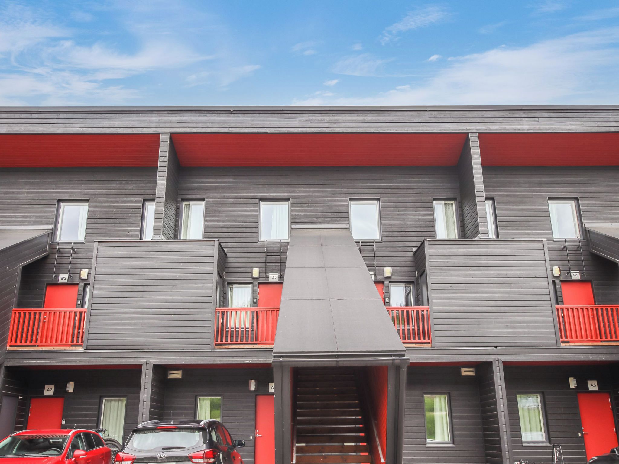 Un edificio de varios pisos con una escalera central, balcones y una puerta roja en cada nivel.