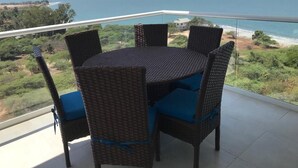 A round table with six wicker chairs, each with blue cushions, on a balcony with a view of the ocean and beach. - Apartamento Amoblado Playa Dormida Santa Marta (Santa Marta)