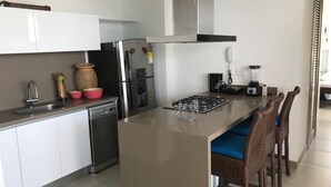 A modern kitchen with white cabinets, stainless steel appliances, a central island with bar stools, and a built-in stove. - Apartamento Amoblado Playa Dormida Santa Marta (Santa Marta)